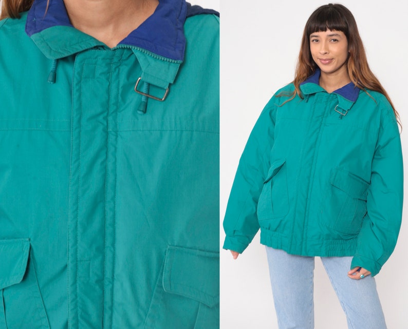 K&ouml;nnte beinhalten: Eine tealblaue Kapuzenjacke mit Rei&szlig;verschluss und zwei Fronttaschen. Die Jacke hat ein marineblaues Futter um die Kapuze.