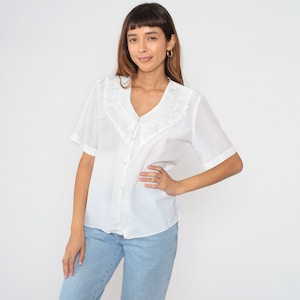May include: A white button-up blouse with a lace collar and short sleeves. The blouse is made of a lightweight fabric and has a relaxed fit.