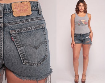 May include: Vintage denim shorts with distressed details, featuring a classic five-pocket design and a Levi's brand patch. The shorts are paired with a gray tank top with a floral graphic. The shorts have a frayed hem.