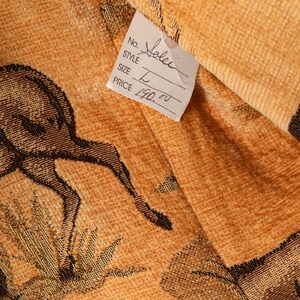 May include: Close-up of a woven textile with a deer design in brown and tan. A white tag displays "Solei" as the style, size "L", and a price. The fabric has a textured appearance.