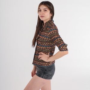 May include: A brown and orange floral print long-sleeve shirt with a collared neckline. The shirt has a button-up front and is worn with black denim shorts.