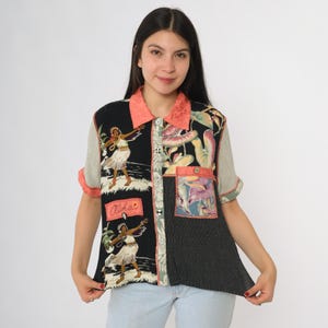 May include: A patchwork short-sleeved shirt with a button-up front. The shirt has panels with a hula dancer print, floral patterns, and vertical stripes. The collar and cuffs are coral-coloured. The word "Aloha" is visible.