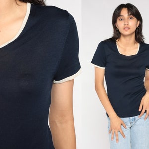 May include: A navy blue short-sleeved t-shirt with a white trim around the neckline and sleeves.