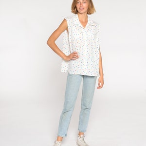 May include: White sleeveless collared shirt with a colorful confetti pattern, paired with light blue jeans and white high-top sneakers. The shirt has a button-down design and a relaxed fit, creating a casual, everyday look.
