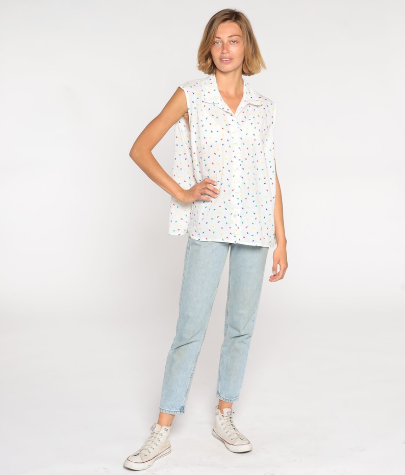 May include: White sleeveless collared shirt with a colorful confetti pattern, paired with light blue jeans and white high-top sneakers. The shirt has a button-down design and a relaxed fit, creating a casual, everyday look.