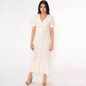 May include: A white ribbed maxi dress with a button-up front and short sleeves. The dress has a v-neckline and a fitted silhouette.
