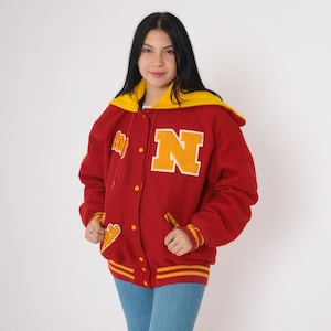 May include: Red varsity jacket with a yellow hood and a large yellow "N" on the front. The jacket has a button closure and yellow and red stripes on the sleeves.