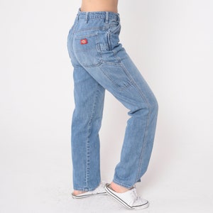 May include: Light blue denim jeans with a red patch on the back pocket. The jeans have a relaxed fit and a straight leg.