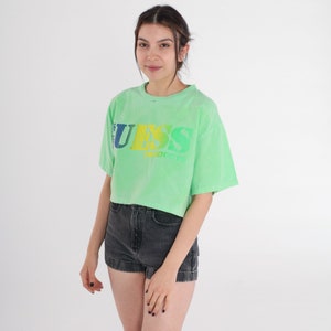 May include: A light green cropped t-shirt with a rainbow coloured "GUESS PRODUCTS" logo.