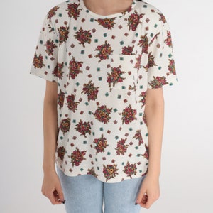 May include: A white short-sleeved t-shirt with a floral print and a small pocket on the left side.