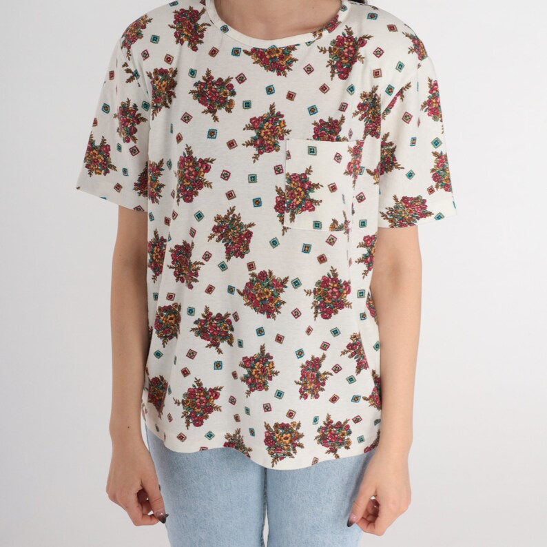 May include: A white short-sleeved t-shirt with a floral print and a small pocket on the left side.