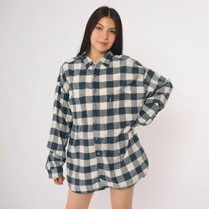 May include: An oversized, long-sleeved shirt with a blue and cream check pattern. The shirt has a button-down front and two chest pockets. The fabric looks soft and woven, ideal for casual wear. The shirt's style is relaxed and comfortable.