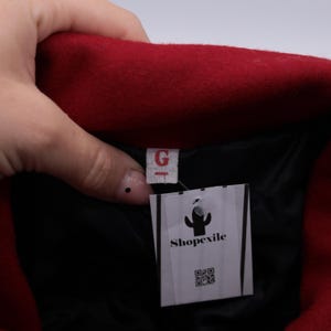 May include: Red wool jacket with a black lining and a white tag that says "Shopexile" with a cactus logo and a QR code.