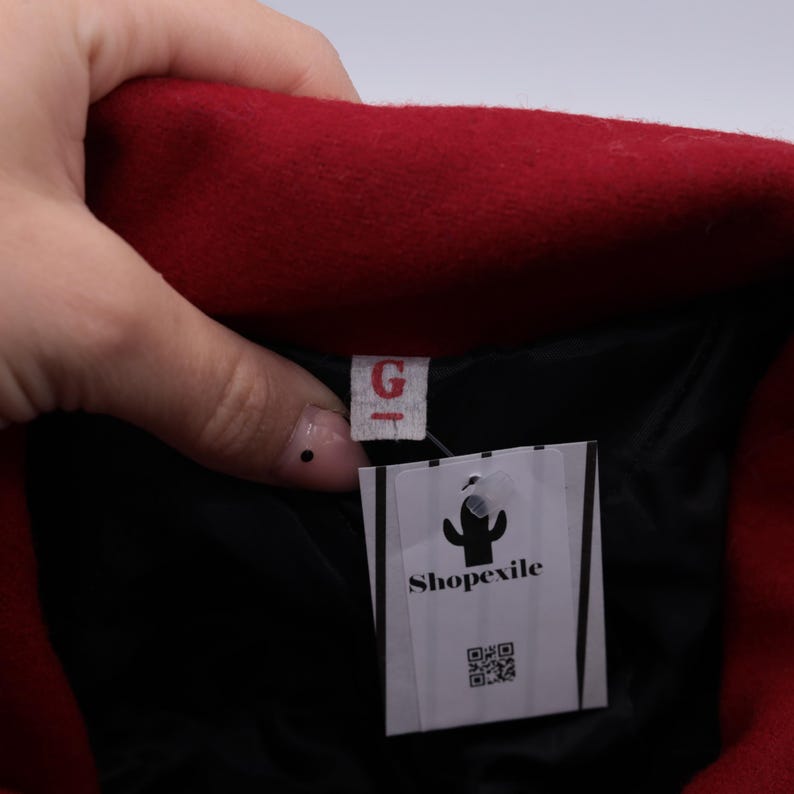 May include: Red wool jacket with a black lining and a white tag that says "Shopexile" with a cactus logo and a QR code.