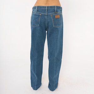 May include: Blue denim jeans with a classic five-pocket design. The jeans feature a straight leg cut and a brown leather patch on the back pocket with the brand name. The jeans are a medium wash and have a traditional button and zipper closure.