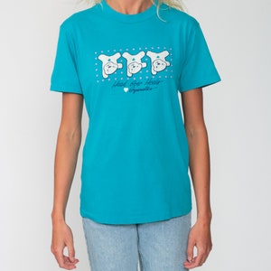 May include: A turquoise blue t-shirt with a graphic of three white bears doing a handstand. The text on the shirt reads "Head Over Heels Gymnastics".