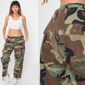 May include: Camouflage cargo pants in shades of brown, green, and black. The pants feature multiple pockets and a relaxed fit. The image shows the pants from multiple angles, highlighting the details of the camouflage pattern and the overall design.