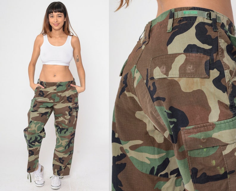 May include: Camouflage cargo pants in shades of brown, green, and black. The pants feature multiple pockets and a relaxed fit. The image shows the pants from multiple angles, highlighting the details of the camouflage pattern and the overall design.