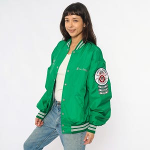 May include: A bright green bomber jacket with white and gray striped trim on the cuffs and collar. The jacket has a button-up front and a patch on the sleeve that reads "World Tournament". The jacket also has the words "Green Garden" embroidered on the front.