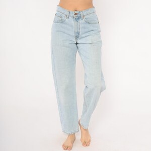 May include: Light blue denim jeans with a classic five-pocket design. The jeans have a straight leg fit and a button and zipper closure. The denim has a faded wash, giving it a vintage look. The jeans are worn at the waist.
