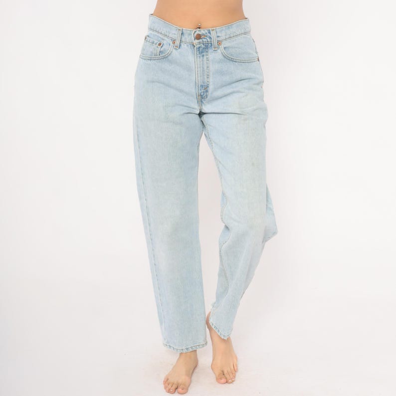 May include: Light blue denim jeans with a classic five-pocket design. The jeans have a straight leg fit and a button and zipper closure. The denim has a faded wash, giving it a vintage look. The jeans are worn at the waist.