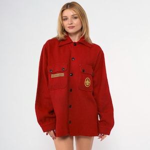 May include: Red long-sleeved button-up shirt with two pockets and embroidered patches. The patches feature the text "Boy Scouts of America" and a scout emblem.