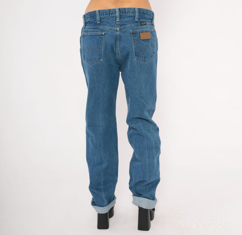 May include: Light blue denim jeans with a classic fit. The jeans feature a straight leg, back pockets, and a brown leather patch. The cuffs are rolled up, and the jeans are worn with black heels. A timeless wardrobe staple.