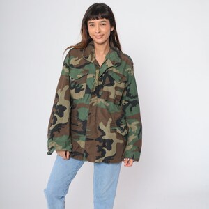 May include: A green, brown, and black camouflage jacket with a button-up front and long sleeves.
