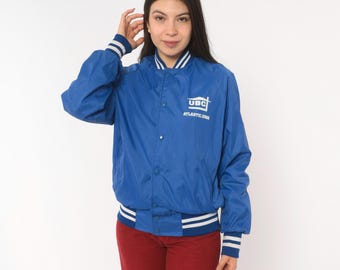 Sportsmaster Varsity Windbreaker uit de jaren 90, koningsblauw, bomberjack met drukknoopsluiting, gestreepte ribboorden, sportieve streetwear, grunge, vintage, maat S.