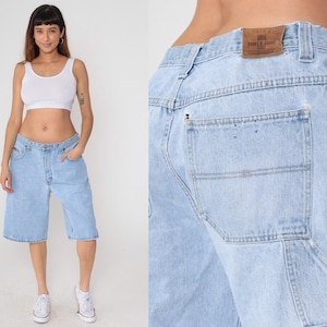 Pode incluir: Calções de ganga azul claro com um corte descontraído. Os calções têm um design clássico de cinco bolsos e fecho de botão e zíper. Usados com um top branco e ténis brancos.