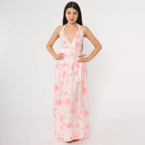 May include: A full-length, halter-neck dress with a white background and a pink floral pattern. The dress features a plunging neckline and a fitted waist with buckle details. The fabric appears to have a slight sheen, and the dress is floor-length.