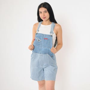 May include: Light blue denim overalls with a striped pattern on the shorts. The overalls have adjustable straps and a single front pocket.