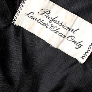 May include: Close-up of a black fabric with a white tag stitched to it. The tag reads "Professional Leather Clean Only" in black script. The tag has a zig-zag stitched border.