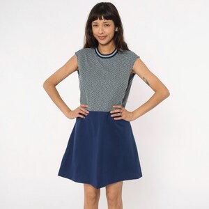 May include: A sleeveless dress with a navy blue skirt and a patterned top in shades of gray and white. The top has a round neckline with a thin blue and white trim. The dress is knee-length and appears to be made of a lightweight fabric.