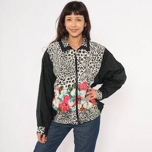 May include: A patterned zip-up jacket with a bold design. The jacket has black sleeves, a collar, and cuffs. The front panel features a floral design, with leopard and zebra prints on the upper sections. The jacket is worn by a person.