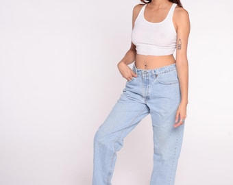Puede incluir: Una mujer con una camiseta sin mangas blanca de canalé y vaqueros azul claro. Los vaqueros tienen un corte recto clásico. El conjunto es sencillo e informal, adecuado para el día a día.