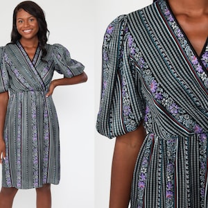 May include: A vintage wrap dress featuring a black and white striped pattern with floral accents in purple and red. The dress has short, puffed sleeves and a V-neckline with black trim. The dress is knee-length.