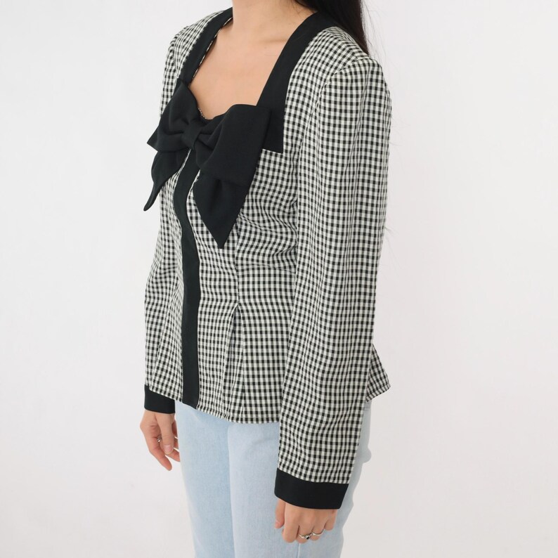 May include: A black and white gingham blouse with a black bow at the neckline. The blouse has long sleeves and a fitted silhouette.