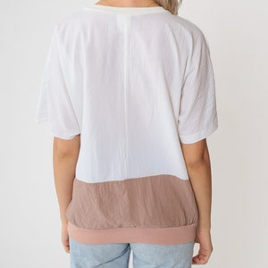 May include: A white and light brown colour block t-shirt with a v-neck and short sleeves.