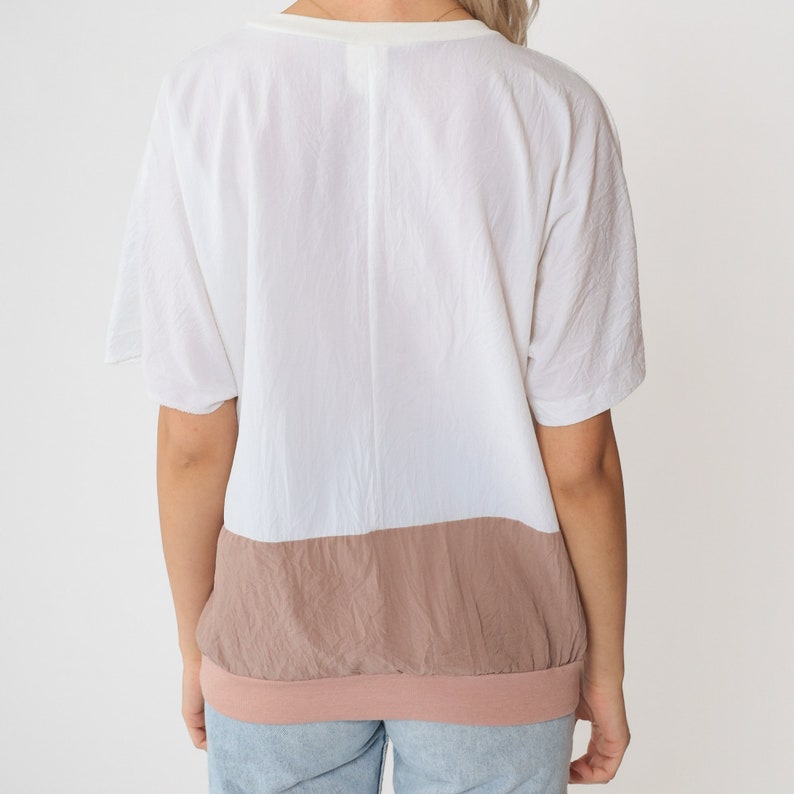 May include: A white and light brown colour block t-shirt with a v-neck and short sleeves.