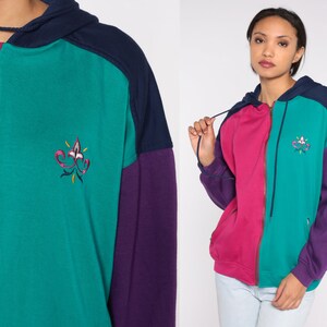 May include: A teal, pink, and purple color block zip-up hoodie with a navy blue hood and a small embroidered design on the front.