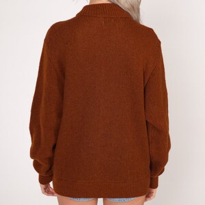 May include: A brown knitted sweater with a high neck and long sleeves.