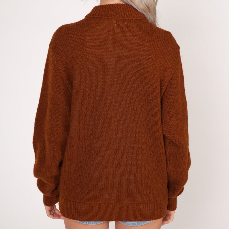 May include: A brown knitted sweater with a high neck and long sleeves.