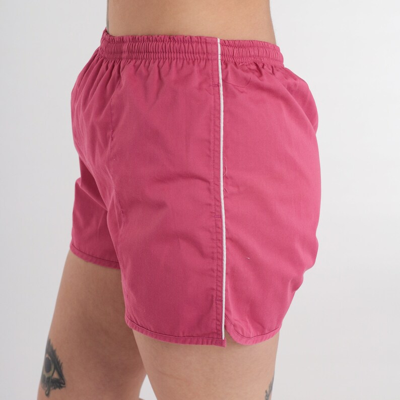 May include: Magenta athletic shorts with a white side stripe. These shorts feature an elasticated waistband and a relaxed fit. Made from a lightweight material, they are suitable for sports or casual wear. The shorts are a vibrant colour.