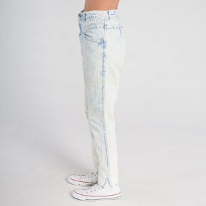 May include: Light blue acid wash jeans with a high waist and a straight leg fit. The jeans have a frayed hem and are shown with white trainers.