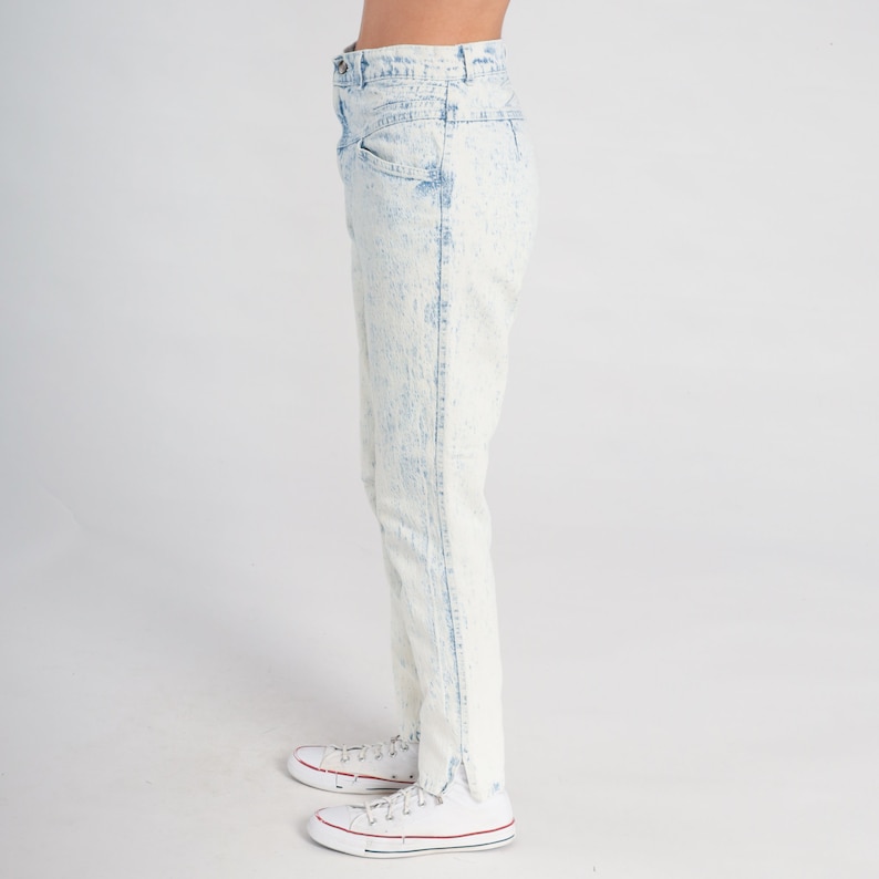 May include: Light blue acid wash jeans with a high waist and a straight leg fit. The jeans have a frayed hem and are shown with white trainers.