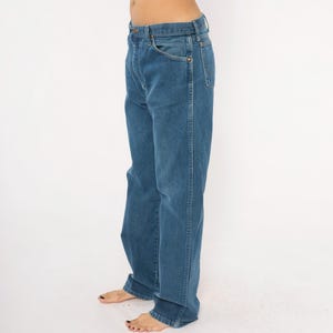 May include: Blue denim jeans with a classic five-pocket design. The jeans have a straight leg cut and a medium wash. The image shows the jeans from the side, highlighting the fit and details of the garment.