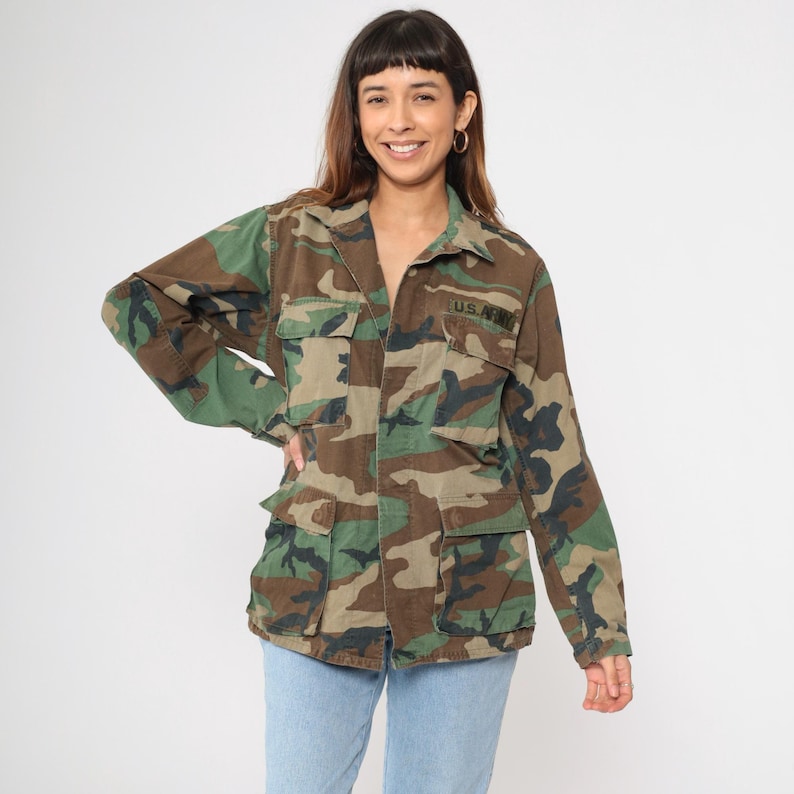 May include: A green, brown, and black camouflage jacket with a button closure and two large pockets. The jacket has "U.S. ARMY" embroidered on the right chest.