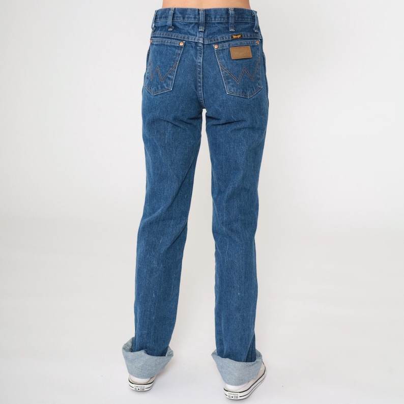 May include: A pair of blue denim jeans with a brown leather patch on the back pocket that says "Wrangler".