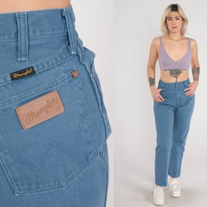Op de afbeelding: Een lichtblauwe spijkerbroek met een hoge taille en een rechte pijp. De broek heeft een bruin leren patch op de achterzak met het woord "Wrangler" erop gedrukt.